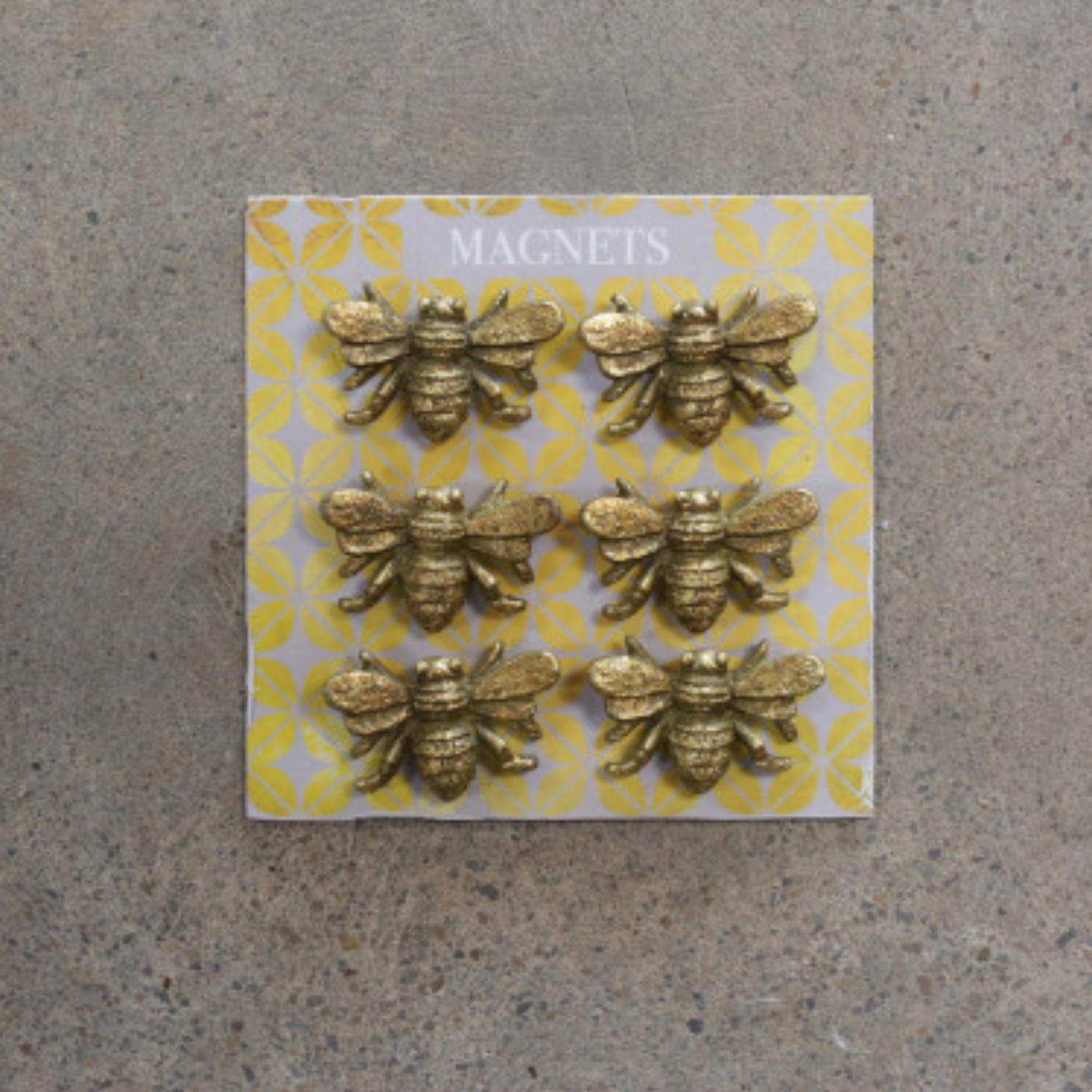 A set of six gold-finished pewter magnets shaped like bees, displayed on a patterned background.